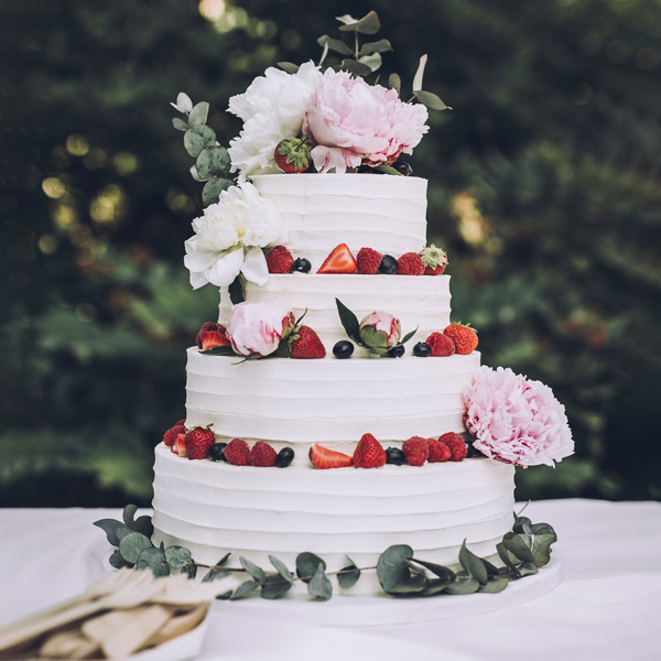 multi tiered event cake decorated with white frosting, berries and fresh flowers